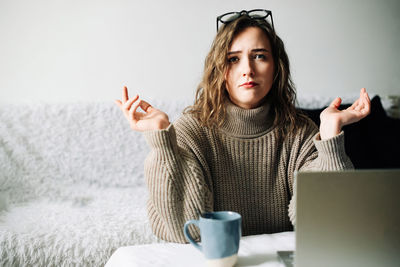 Portrait of young woman using mobile phone while standing against wall