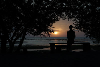 Rear view of silhouette man standing by sea against sunset sky