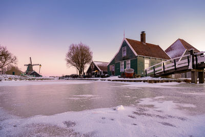 Snow covered houses by buildings against sky during winter