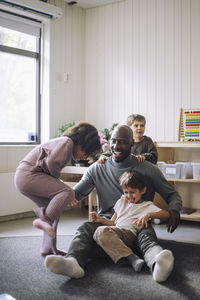 Playful kids having fun with male teacher sitting in classroom at kindergarten