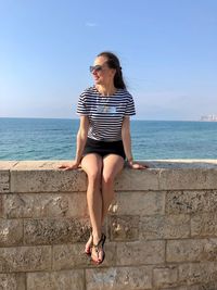 Smiling mid adult woman sitting on retaining wall with sea in background