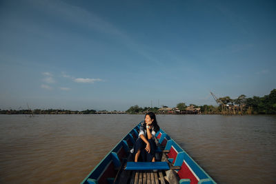 Man sitting on boat in river against sky