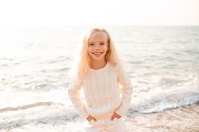 Happy smiling child girl 7-8 year old wear white knitted sweater and pants posing over nature sea