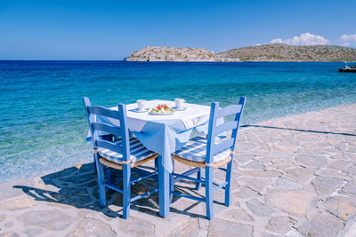 Chairs on table by sea against blue sky