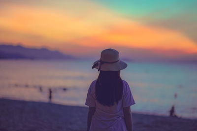 Rear view of woman standing at beach during sunset