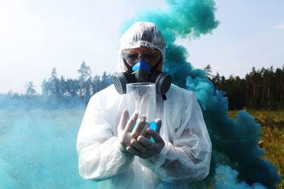 Portrait of scientist with liquid standing against blue smoke