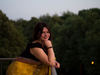 Portrait of smiling young woman against trees