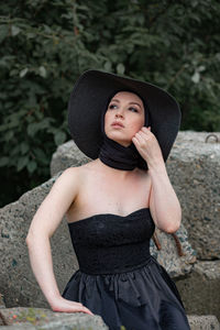 Woman wearing black dress and hat sitting on rock