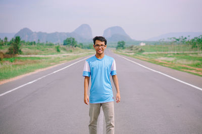 Portrait of man standing on road against clear blue sky