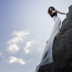 Low angle view of woman in evening gown standing on rock against sky