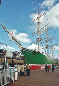 People on sailboats moored at harbor against sky