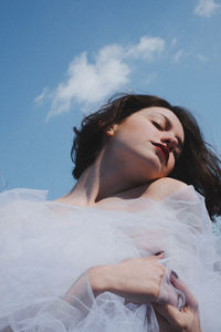 Low angle view of young woman in white dress against sky