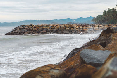 Rocks on shore by sea against sky