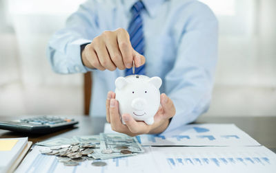 Midsection of businessman putting coin in piggy bank
