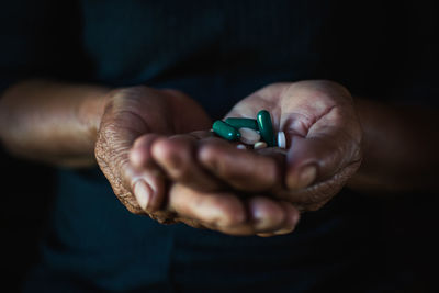 Close-up midsection of woman holding medicines against black background