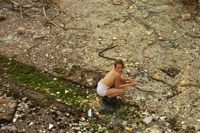 High angle view of topless woman crouching amidst broken glasses
