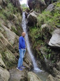 Full length of woman standing on rock against waterfall