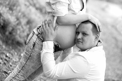 Man embracing pregnant wife abdomen outdoors