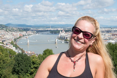 Portrait of smiling mature woman wearing sunglasses while standing against sky in city