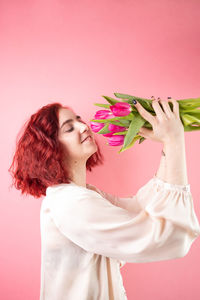 Young woman holding bouquet against pink background