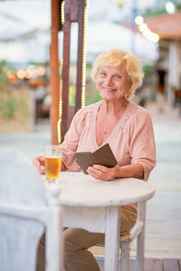 Mature woman sitting at a table in a summer cafe and drinking beer