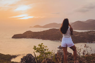 Rear view of woman standing by sea against sky during sunset