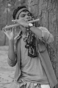 Man playing flute while standing against tree trunk