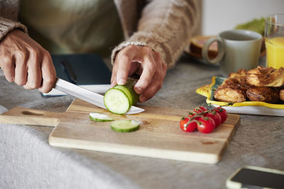 Man's hand cutting cucumber on wooden chopping board