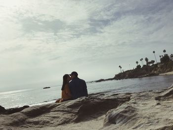 Rear view of men sitting on beach against sky