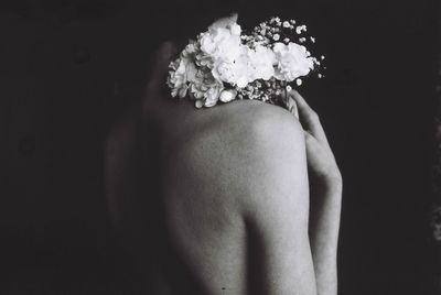 Shirtless woman with bouquet standing against black background