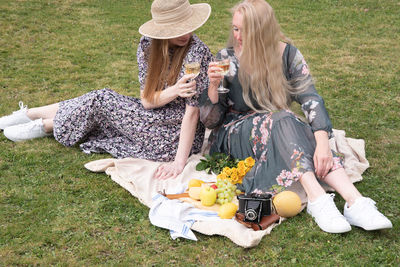 Two young women in a summer long dresses is resting on a picnic,blanket on grass