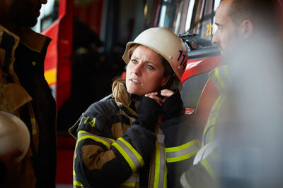 Female firefighter wearing helmet while talking with other coworkers in fire station