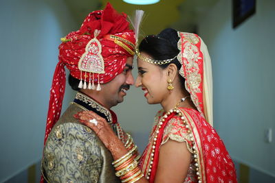 Smiling bride and groom looking face to face against wall at home