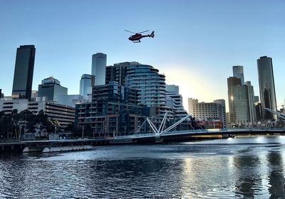 Helicopter flying over river and buildings against sky