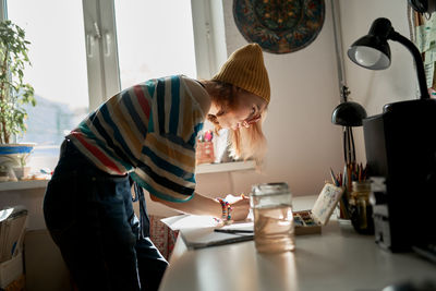 Side view of delighted female artist in trendy wear creating artwork in studio while painting on paper with watercolors