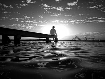 Silhouette man in sea against sky during sunset
