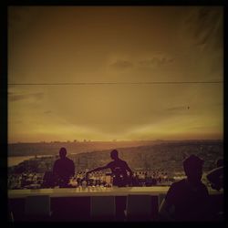 Silhouette people sitting by sea against sky during sunset