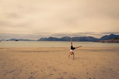 Woman doing handstand on shore at beach against sky