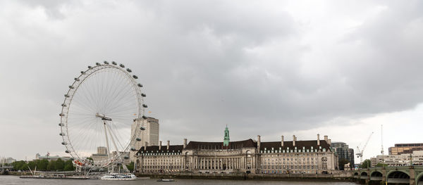 Millennium wheel by thames river against sky