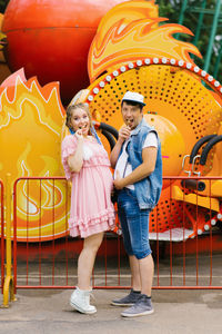 Funny future parents eat lollipops and show each other their bellies at an amusement park