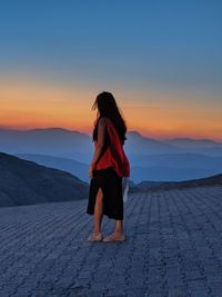 Rear view of woman standing at beach against sky during sunset