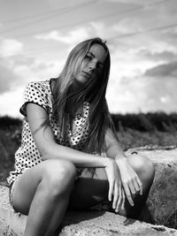 Portrait of young woman sitting on retaining wall against sky