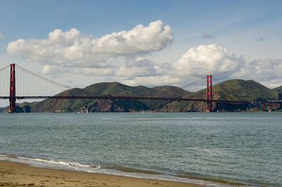 View of suspension bridge over sea against cloudy sky