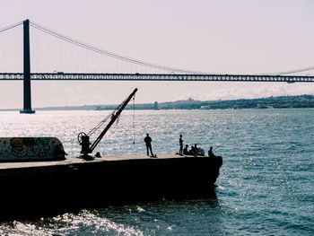 Silhouette people fishing in sea against clear sky