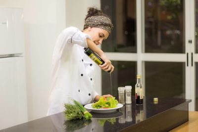 Female chef pouring olive oil on salad while standing in commercial kitchen