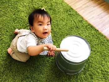 High angle portrait of baby boy playing with bucket and rolling pin on carpet at home