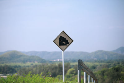 Road sign on field against sky