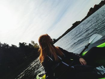 Tilt image of woman looking away while sitting in boat on river against sky