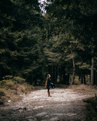 Side view of woman standing on road in forest