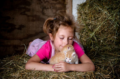 Young  girl in overalls, cuddles with kittens in the barn on bales of straw